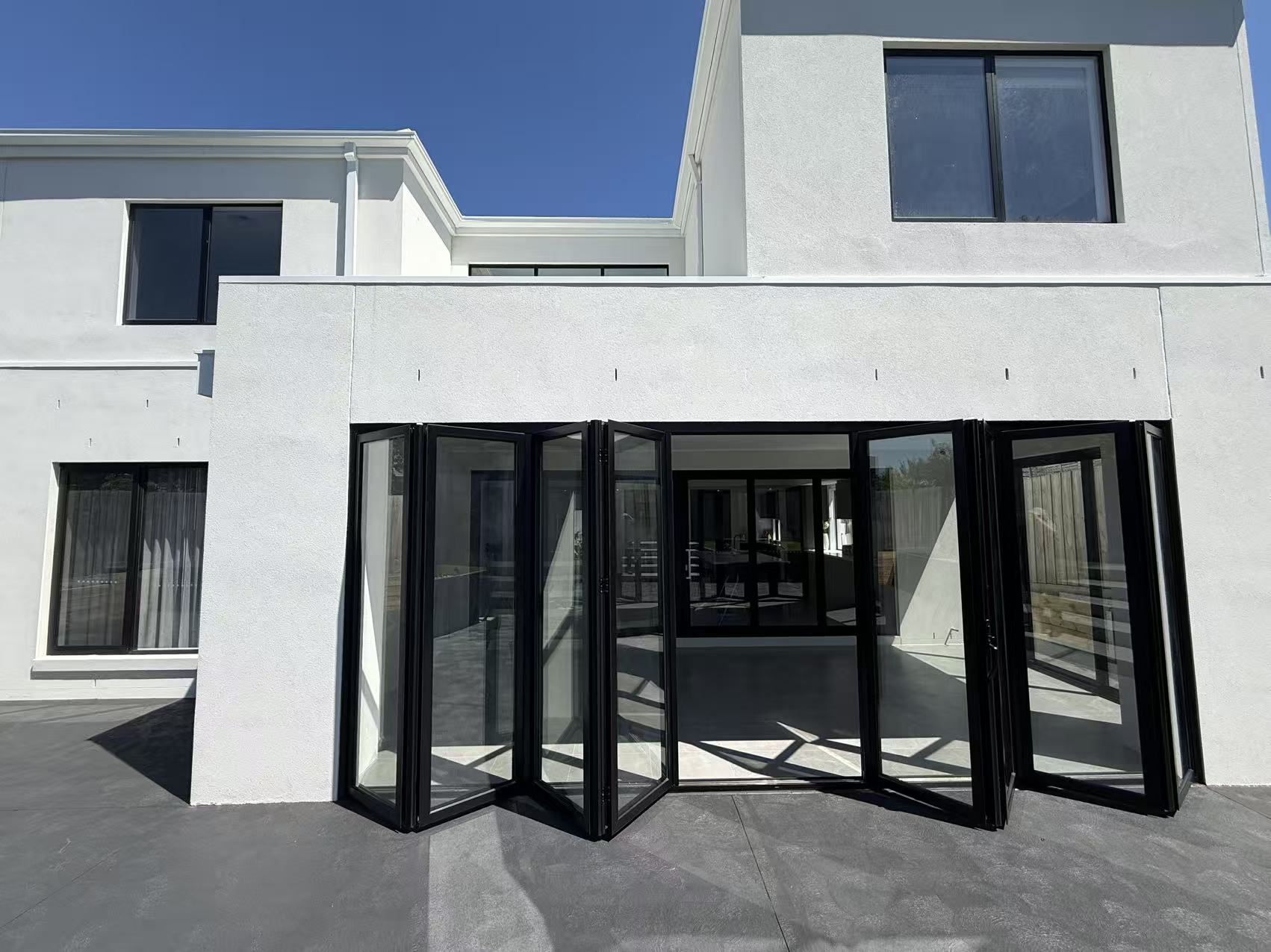 Wide black aluminium bi-fold door system opening to an outdoor area